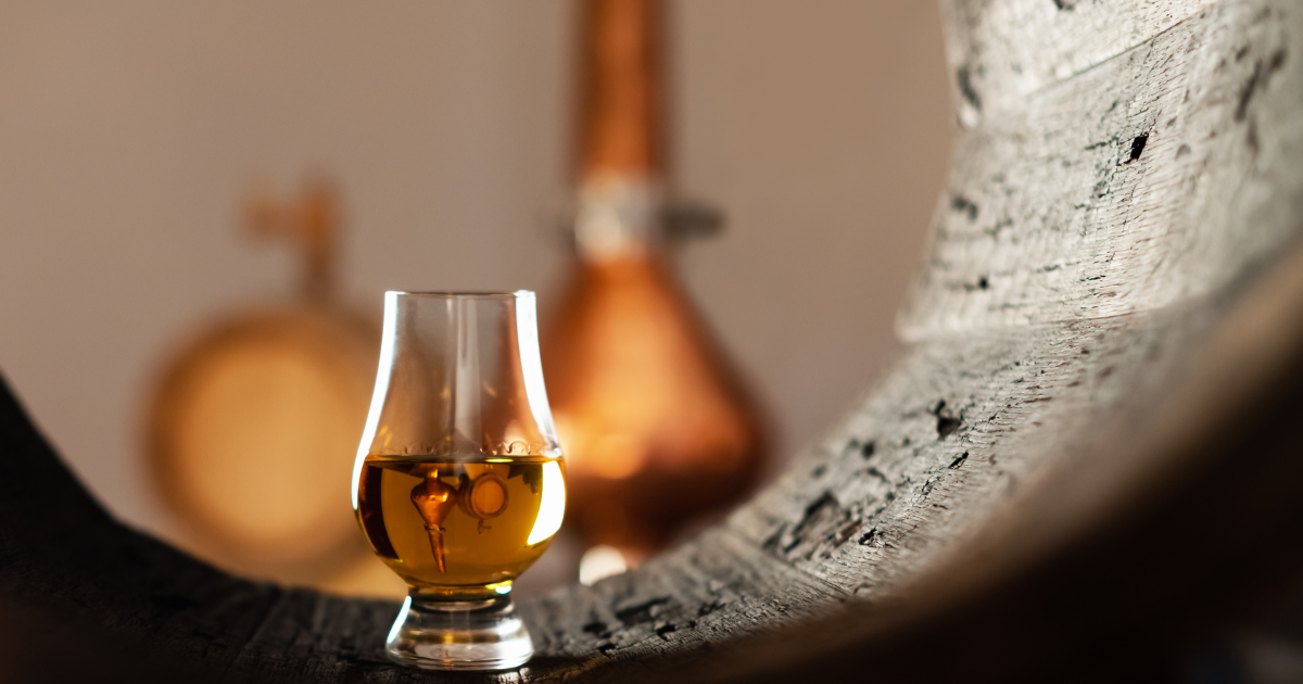 A glass of whisky inside a barrel with stills in the background