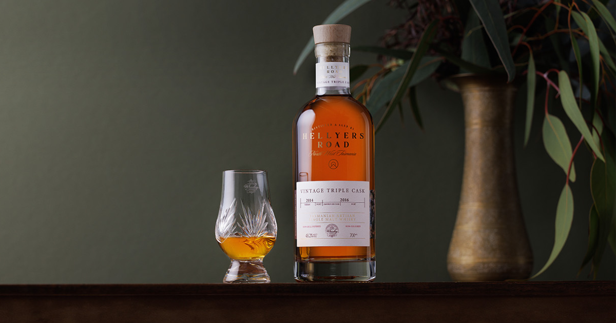 A bottle of Hellyers Road Vintage Triple Cask on a table with a glass in front of a vase of flowers