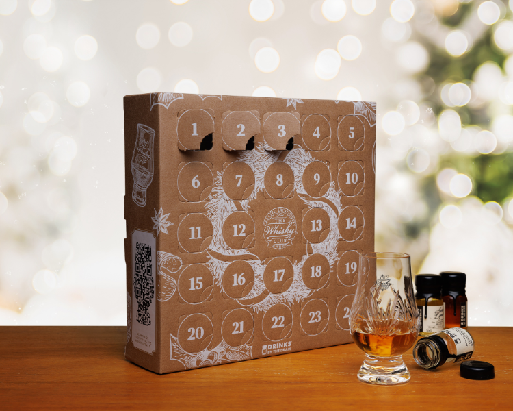  A whisky advent calendar and a Glencairn of whisky on a table with a Christmas lights in the background 