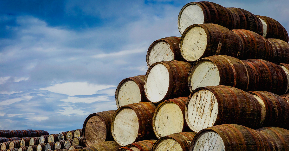 The World's Best Cask Finishes You Need To Try A bootle of whisky barrels stacked against a blue sky