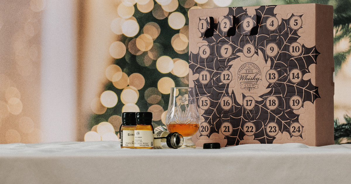 A whisky advent calendar and a Glencairn of whisky on a white table cloth with a Christmas tree in the background 